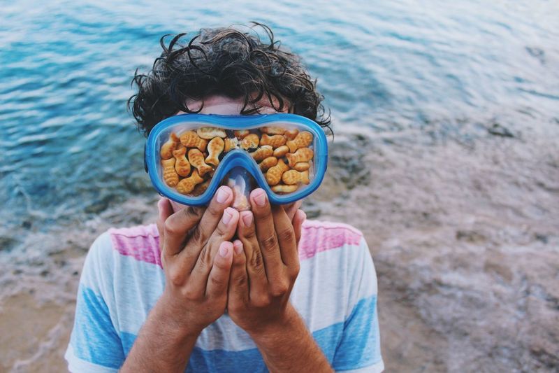 Close-up of man wearing swimming goggles with fish food at beach