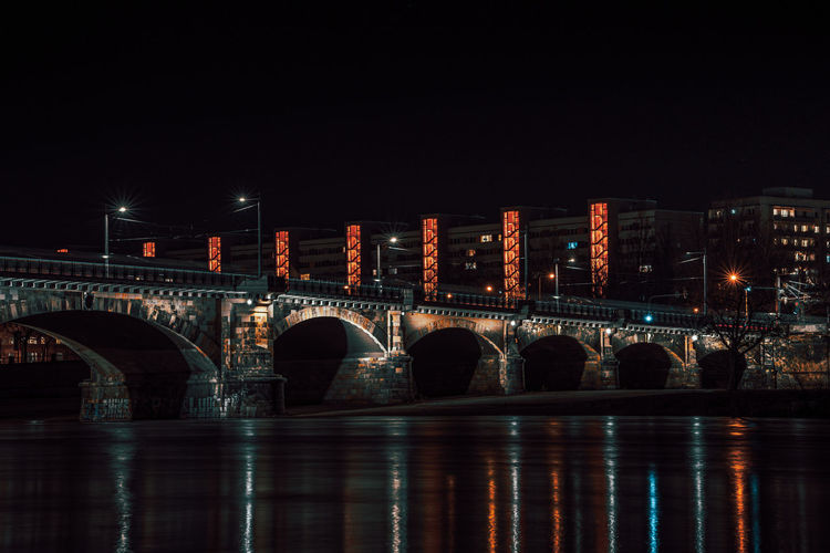 Arch bridge over river against sky in city at night