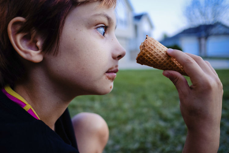 Side view of girl looking at ice cream cone while sitting in yard