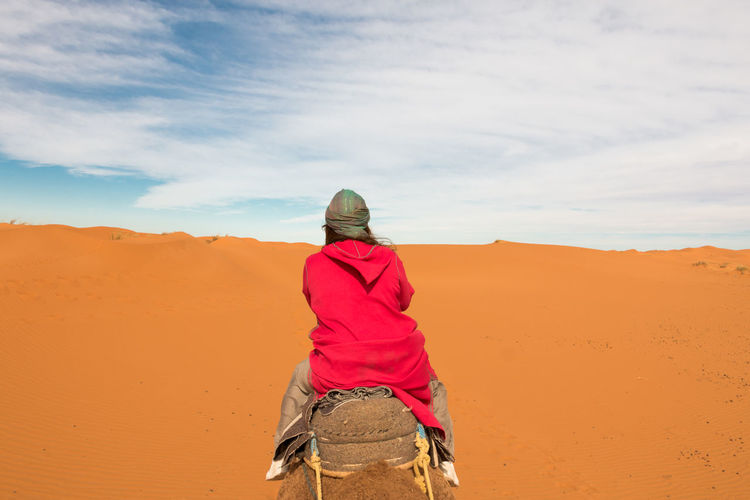 Woman with pink djellaba riding a camel among the dunes of the desert