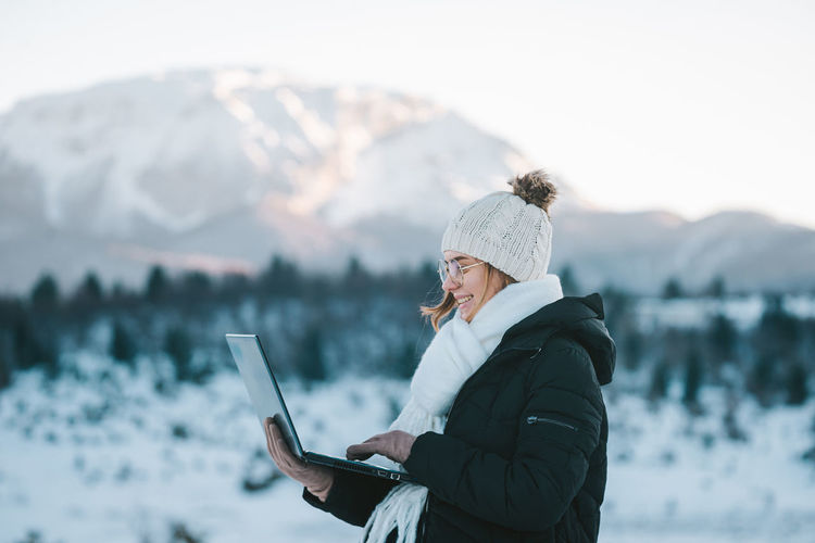 Side view of smiling woman using laptop on snow covered land