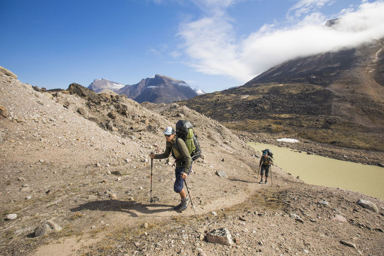 Backpackers hike up a mountain ridge in akshayak pass, baffin island.