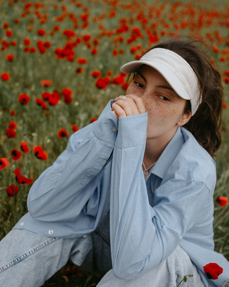Attractive young woman sitting in the poppy field with flowers in blue shirt and jeans