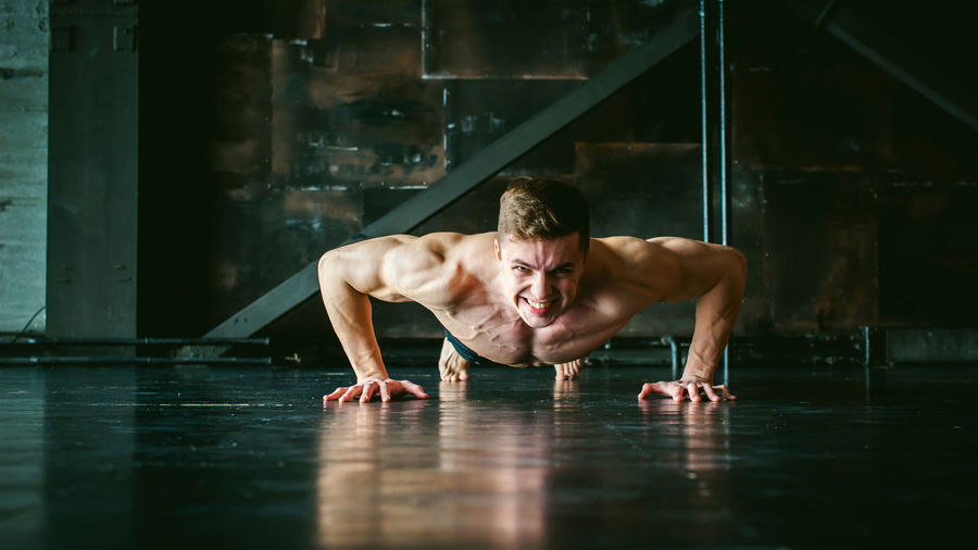 Portrait of shirtless muscular man doing push-ups at home
