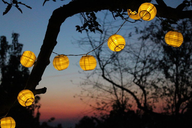 Low angle view of illuminated lanterns against sky at sunset