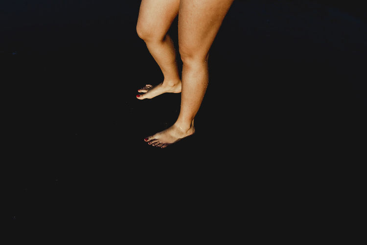 High angle side view of crop anonymous barefoot female standing on dark beach at night