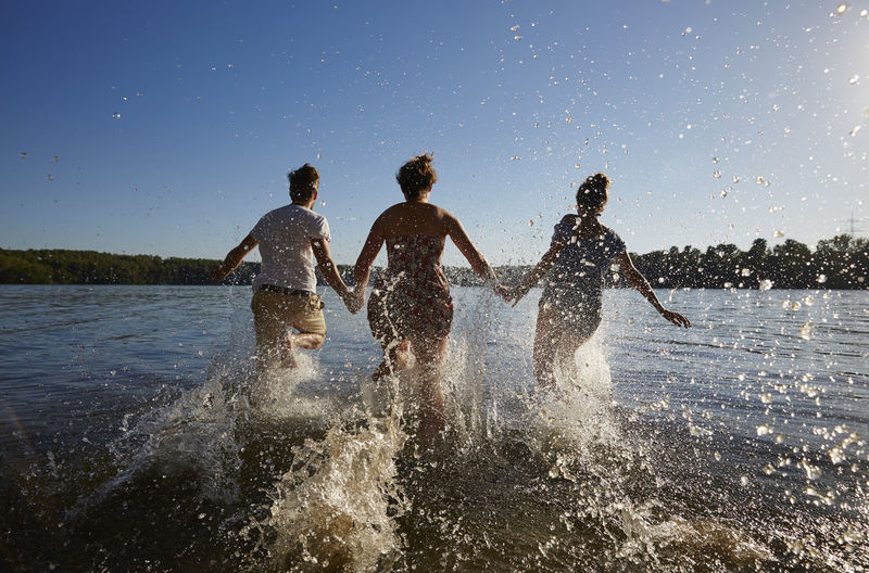 Back view of friends running in a lake