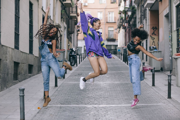 Full length of female friends jumping on street in city