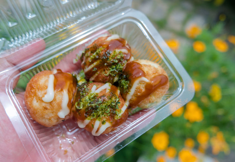 Cropped hand holding takoyaki in plastic container
