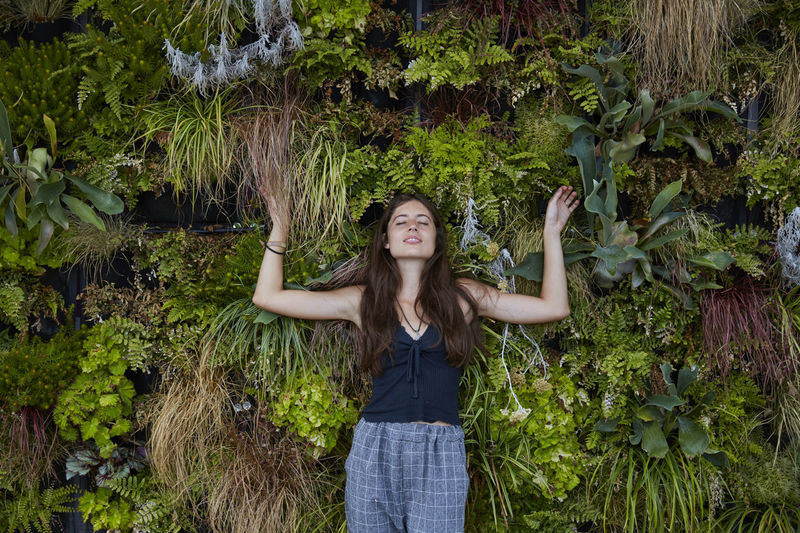Portrait of smiling young woman with closed eyes in front of plant wall