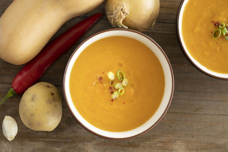 Top view bowl with delicious pumpkin soup, ingredients pumpkin, potato, garlic, pepper wooden table