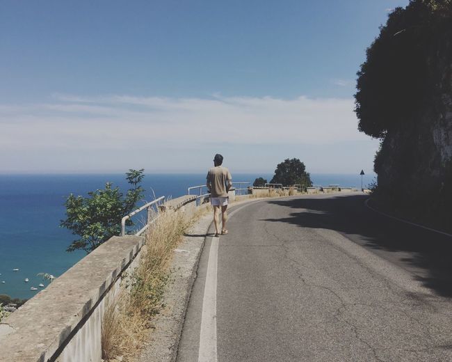Rear view of man on road by sea against sky