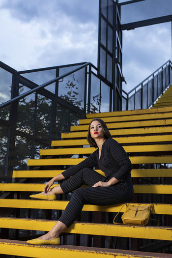 Young woman sitting on staircase against sky
