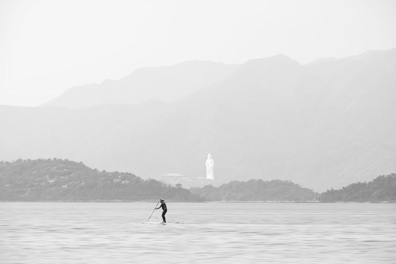 Man on sea by mountain against sky
