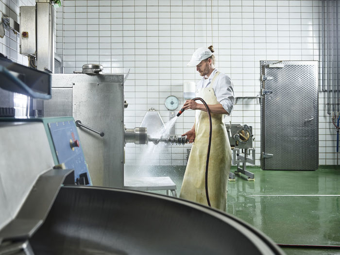 Butcher wearing apron washing machinery in factory