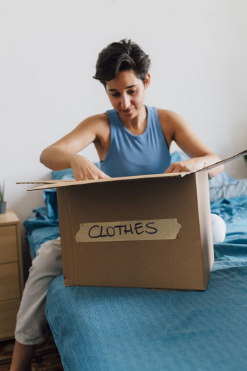 Young woman packing donation box in bedroom