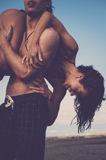Midsection of shirtless man carrying girlfriend over shoulder at beach 